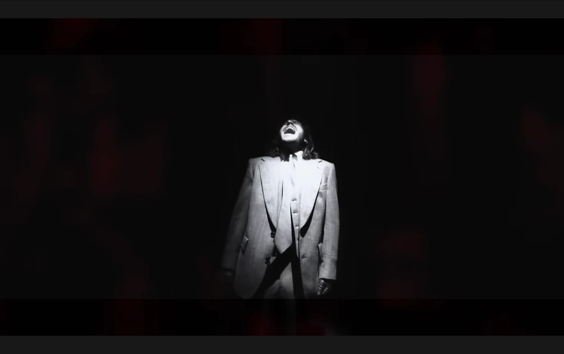 Black and white music video frame of a suited figure under a spotlight